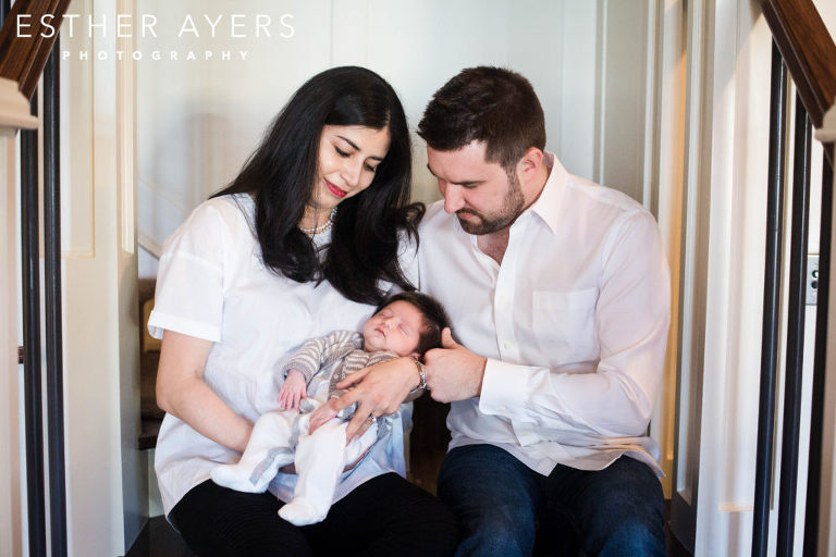 mom and dad looking at newborn baby boy on staircase